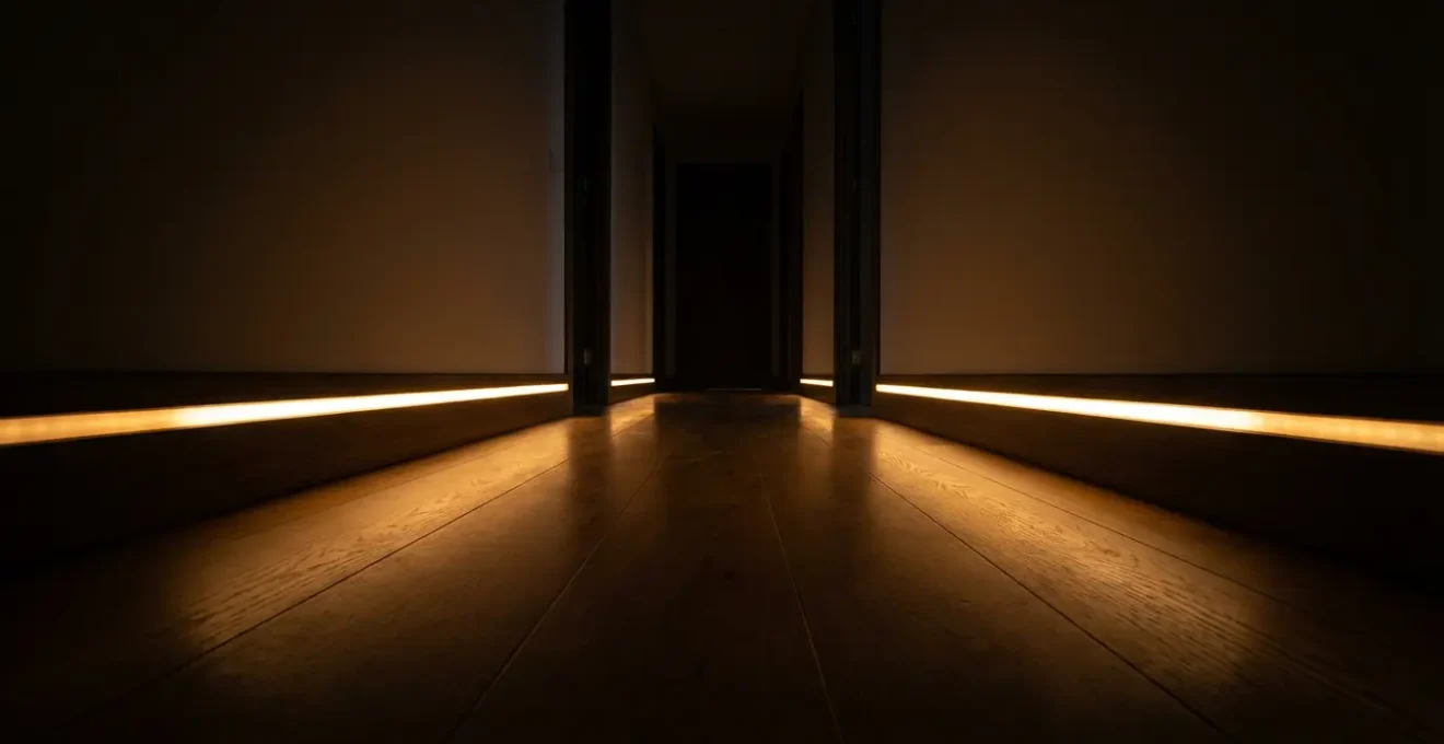 Couloir avec balisage LED ambré discret le long des plinthes créant un chemin lumineux sécurisé